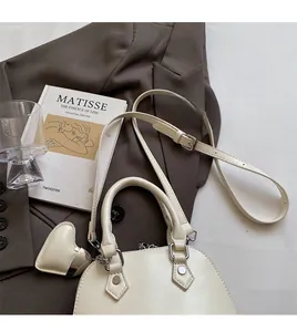 Top-down view of white shell bag with heart charm and detachable adjustable shoulder strap