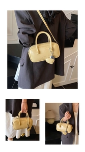 Detail of yellow bowling bag with top handles, crossbody strap, and heart charm accessory