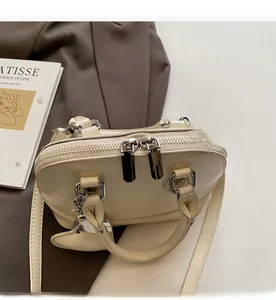 Detailed top view of beige shell-shaped handbag with smooth dual metal zippers