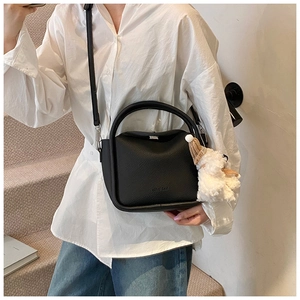 Détail d'un sac à main noir en cuir grainé avec un charme en peluche blanche et bandoulière