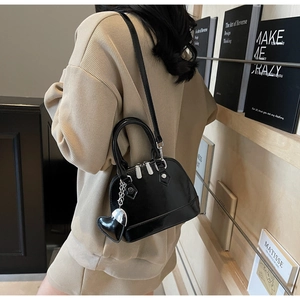 Detail of a black glossy shell bag with silver heart charm and adjustable shoulder strap