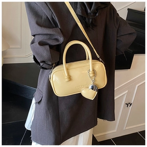 Close-up of creamy yellow patent leather bowling bag with heart charm and slim strap