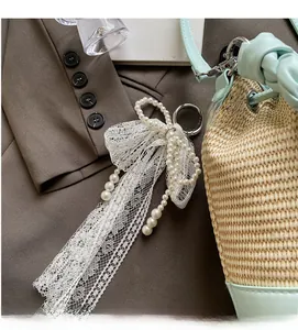 Detailed view of elegant white lace and pearl bow charm accessory on a woven bag