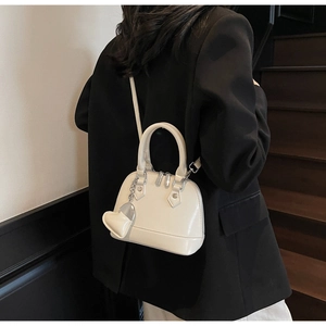 Close-up of cream dome bag featuring silver studs and heart charm on a model