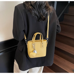 Detail of small yellow bucket bag with silver heart charm and pebbled leather texture