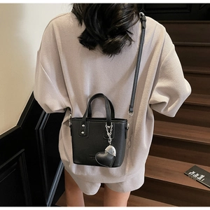 Close-up of black litchi pattern leather bucket bag with silver heart pendant and strap