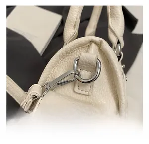 Dettaglio di ganci in metallo argento e anello a D su borsa in pelle beige testurizzata