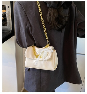 Close-up of cream square bag with gold chunky chain and lace bow with pearl detail