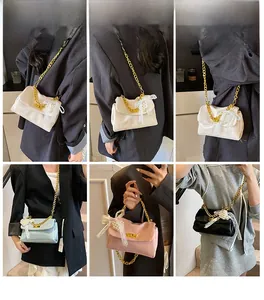 Detail of elegant small square bag with chunky gold chain and lace pearl bow charm