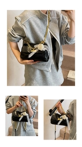 Close-up of black square bag featuring gold chain, lace bow, and pearl flower charms