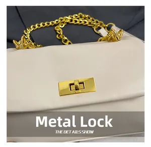 Close-up of golden hardware lock and chain on a cream quilted square shoulder bag