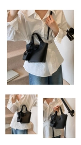 Detail of black lychee grain bucket bag featuring twin handles and mini charm