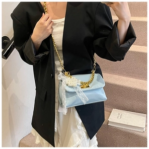 Detail of light blue crossbody bag with gold chain and pearl heart charm on a model