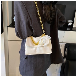 Detail of off-white crossbody bag with gold chain, lace bow, and pearl charm accents