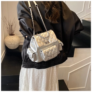 Rear view of silver quilted backpack with metal chain straps worn by a model