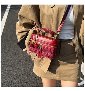 Detail of red tweed and leather box bag with cherry charm accessory on asphalt background