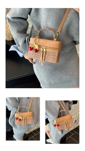Detail of tweed and leather crossbody box bag with cherry charm on a grey dress