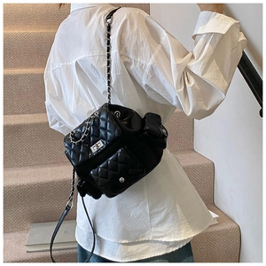 Close-up of a black quilted leather backpack featuring silver chain straps on a model
