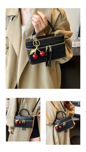 Detail view of black lychee leather and tweed box bag with cherry charm and gold zipper