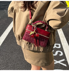 Detail of burgundy leather and tweed crossbody bag featuring a cherry charm and gold zipper