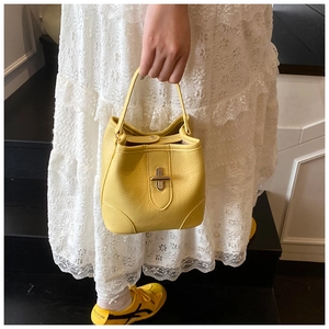 Detail of bright yellow bucket bag with lychee texture and metallic turn-lock closure