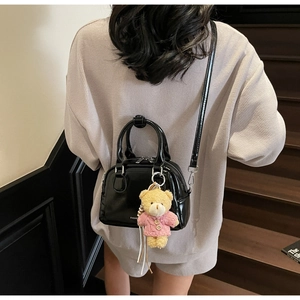 Dettaglio della mini borsa bowling nera lucida con ciondolo a forma di orso sul modello