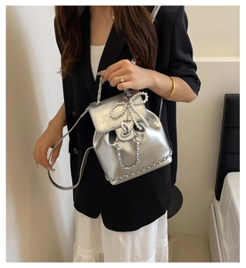 Detail of silver chain bag featuring pearl bow and heart charm on modern textured leather