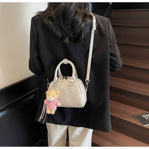 Borsa bowling bianco sporco con ciondolo orso rosa indossata su un blazer nero su scale