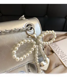 Detail of silver metallic backpack featuring a pearl bow and silver heart pendant charm