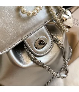 Detail of silver metallic bucket bag featuring pearl handle and heart pendant charm