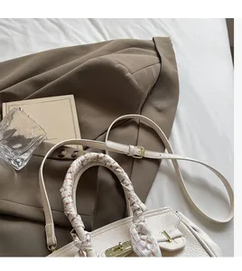 Detail of cream lychee leather handbag with silk scarf handle on stylish white bedding