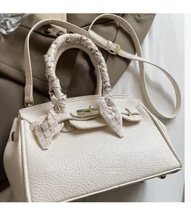 Detail of off-white lychee leather handbag with golden twist lock and decorative silk scarf