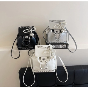 Detail of three mini backpacks in black, silver and white with pearl bow and chain