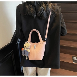 Pink pebbled leather bucket bag with silver clasp and bear charm on wooden stairs