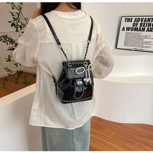 Rear view of a model wearing a mini black leather backpack with silver chain and pearl bow