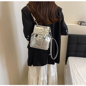 Silver metallic mini backpack featuring pearl bow detail and chain straps on model