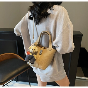 Detail of lychee pattern leather bucket bag with metal turn-lock and teddy bear charm