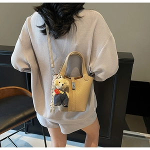 Beige litchi grain bucket bag styled with bear charm and silk scarf on a model