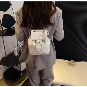 Detailopname van witte lederen rugzak met parelstrikn en metalen ketting op een model