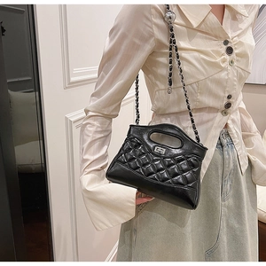 Model wearing a black quilted leather crossbody bag with chain strap and cutout handle