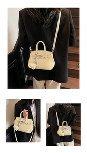 Detail view of a cream Kelly-style handbag with top handles and heart charm accessory