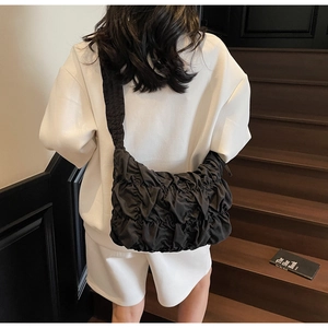 Detail view of black pleated cloud bag texture on model wearing white sweatshirt