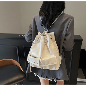 Detail of cream white bucket backpack with chain straps on a model wearing grey blazer