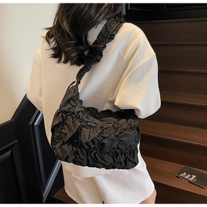 Detail of black cloud bag with pleated texture shown on model in minimal white suit