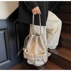 Close-up of beige drawstring bucket bag featuring silver rivets and chain strap detail