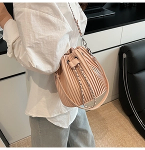 Detail of light pink bucket bag featuring accordion pleats and leather chain strap