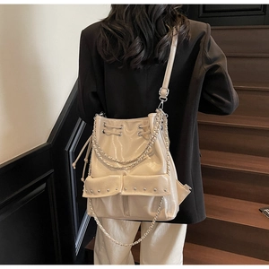 Detail of beige high-gloss bucket bag with silver chains and rivets on wooden stairs