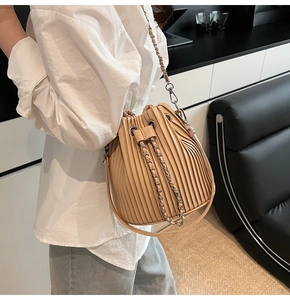 Macro view of beige pleated bucket bag with fine vertical folds and gold chain strap