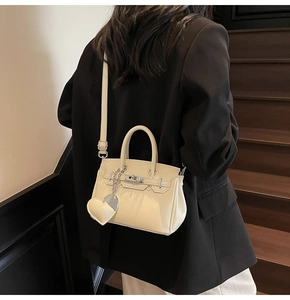 Detailed side view of a cream mini handbag with shiny leather and heart charm