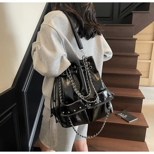 Detail of glossy black leather bucket bag featuring metal chain and silver rivet accents